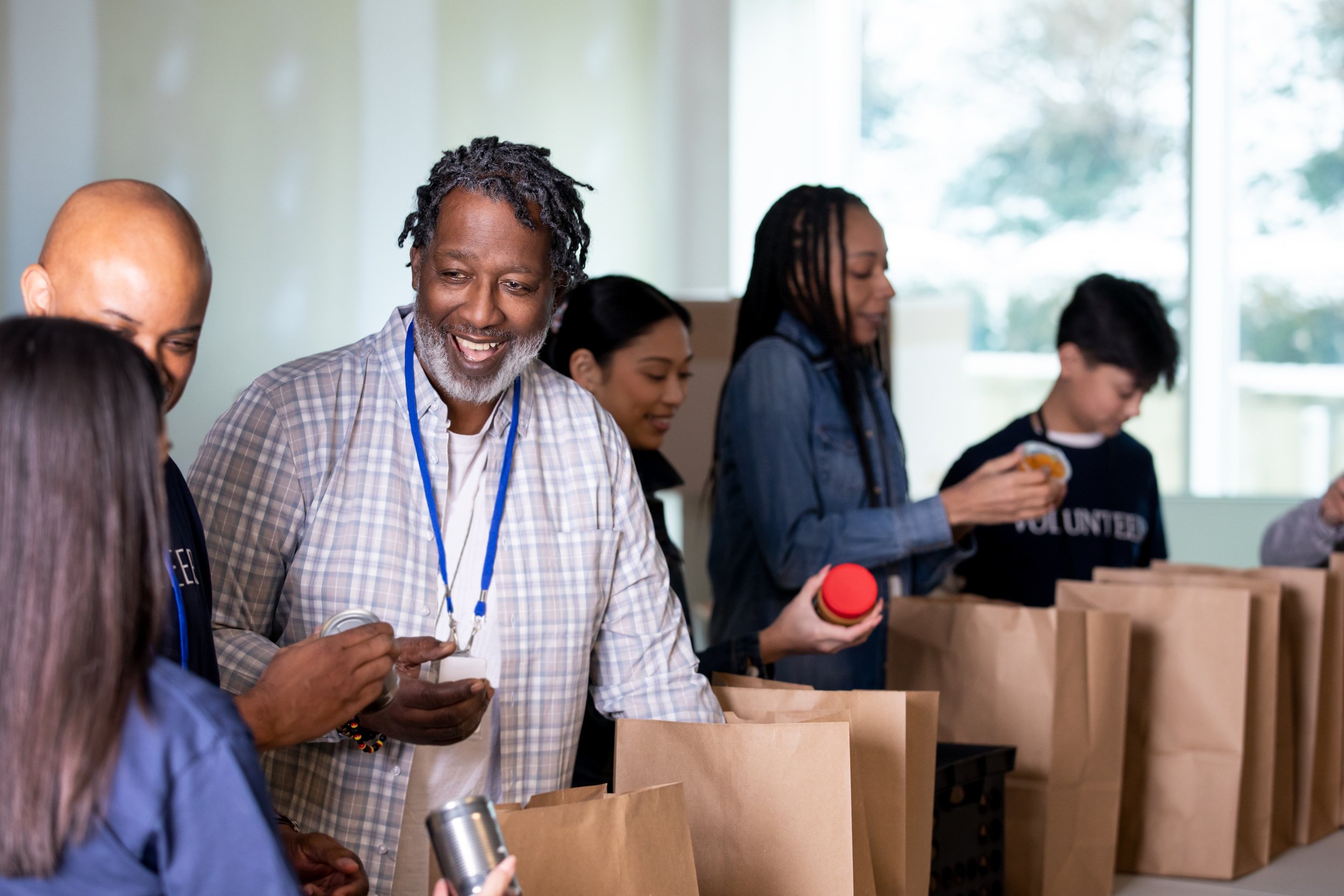 Senior man volunteering with group of people to package food donations at community outreach center